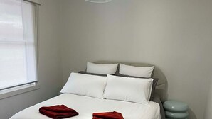 A neatly made bed with white bedding and two red towels, a light-colored headboard, and a modern pendant light.