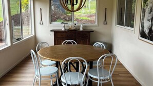 A dining area with a round wooden table surrounded by white chairs, a wooden floor, and a ceiling light fixture.