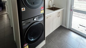 A compact laundry room with two stacked washers and dryers, a small sink, and a window with a view of the outdoors.