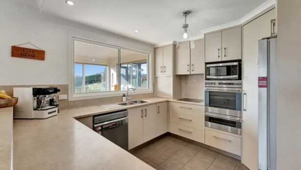 A modern kitchen with a large window, stainless steel appliances, and light-colored cabinetry.