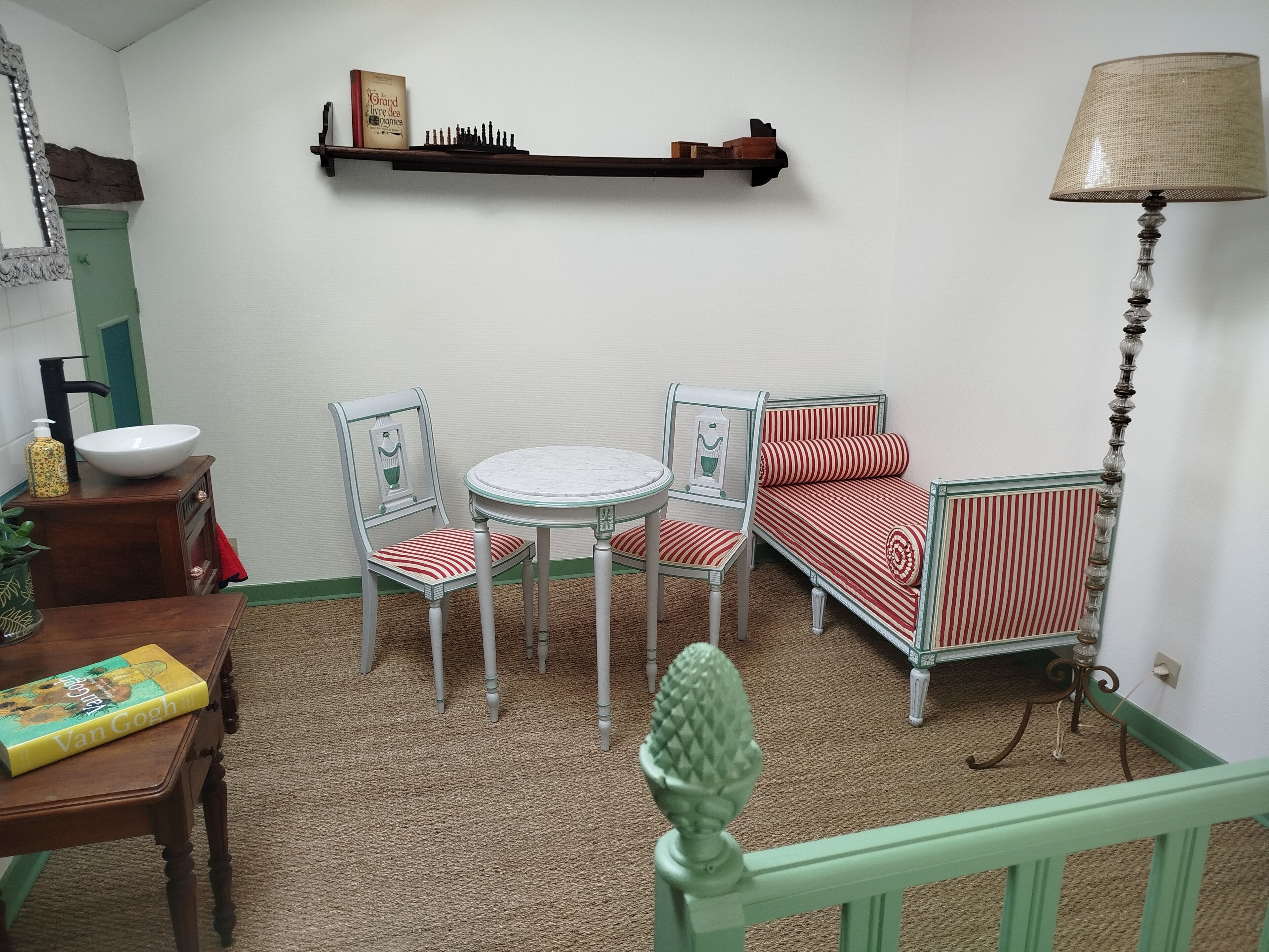 Et hyggeligt rum med et rundt bord, to stole, en lille sofa, en bogreol, en lampe og et dekorativt spejl.