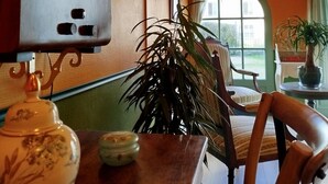 Un coin repas avec une table en bois, des chaises, une plante en pot, une horloge murale et une fenêtre avec des rideaux.