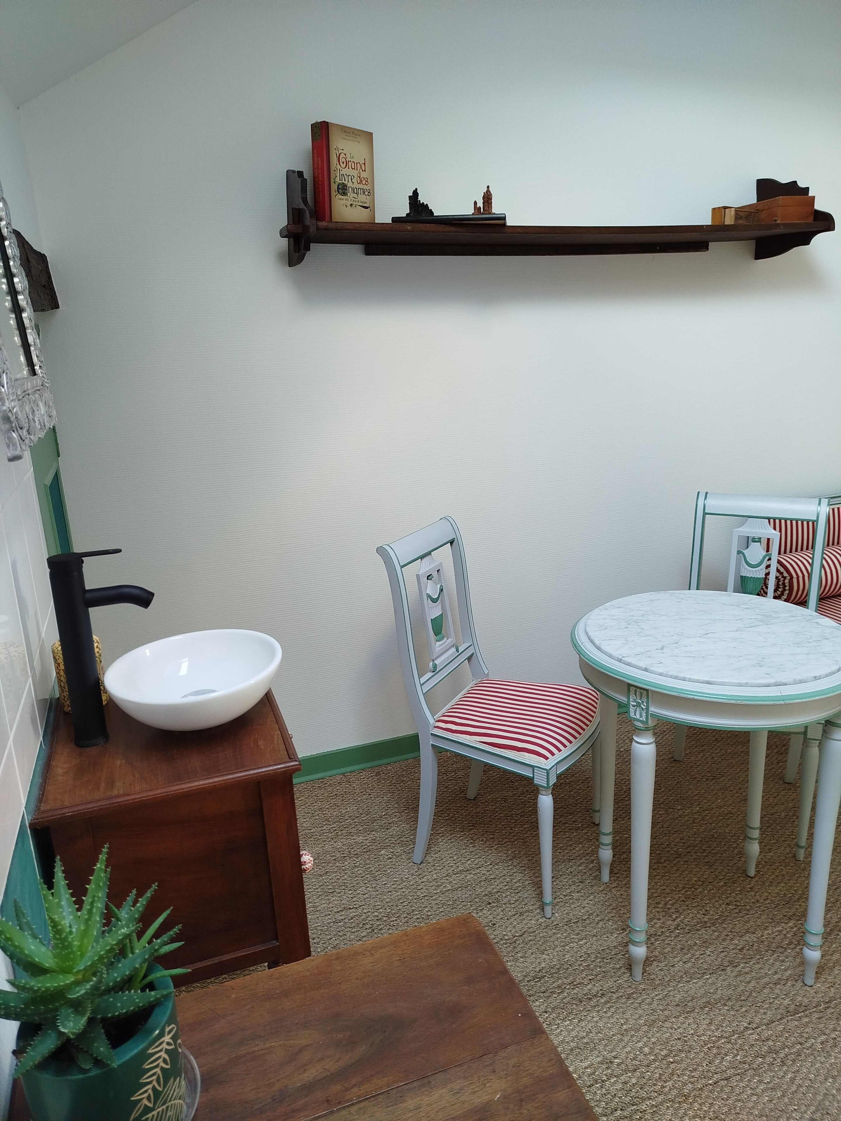 Una habitación pequeña y acogedora con una mesa de madera, una silla, un estante con adornos y una planta en maceta.