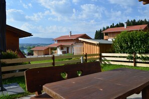 Un banc et une table en bois, placés dans un cadre extérieur ensoleillé, avec vue sur des maisons et des montagnes.