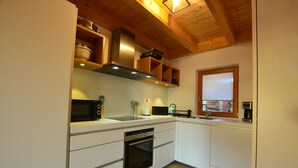 Eine moderne Küche mit weißen Schränken, einem eingebauten Backofen, einer Mikrowelle und Holzregalen über der Arbeitsfläche.
