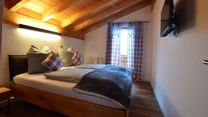 Ein Schlafzimmer mit Holzboden, einem Bett mit vielen Kissen, einem Nachttisch und einem an der Wand befestigten Fernseher.