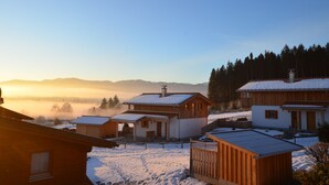 Ein verschneites Dorf mit Holzhäusern, wolkenlosem Himmel und Bergen im Hintergrund.
