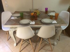 A dining table set with plates, cutlery, and a fruit bowl. - 🏖Sunny Family Studio • 60m Walk to Beach • Parking & Garden (Skala Marion)