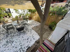 An outdoor patio with a table and chairs, surrounded by white pebbles and plants. - 🏖Sunny Family Studio • 60m Walk to Beach • Parking & Garden (Skala Marion)