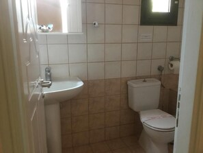 Et lille badeværelse med en hvid vask, toilet og et vindue over vasken.