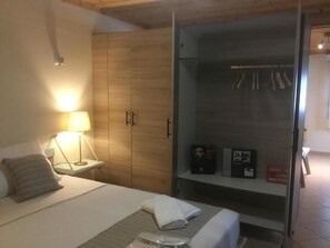 A hotel room with a bed, a nightstand with a lamp, a wardrobe, and a shelf with items. - 🏖Sunny Family Studio • 60m Walk to Beach • Parking & Garden (Skala Marion)