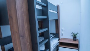 Een compacte slaapkamer met een stapelbed, inbouwschappen, een nachtkastje en een kleine potplant.