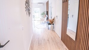 Een moderne hal met houten vloer, een zwarte deurmat en een wand van houten panelen.