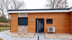 Een modern gebouw met een houten gevel, een accentmuur van natuursteen, een zwarte deur en een airconditioner.