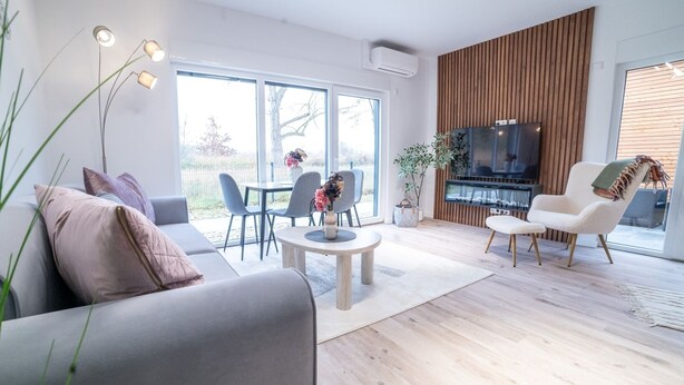 Een moderne woonkamer met een grijze bank, een eettafel met stoelen, een televisie en een open haard.