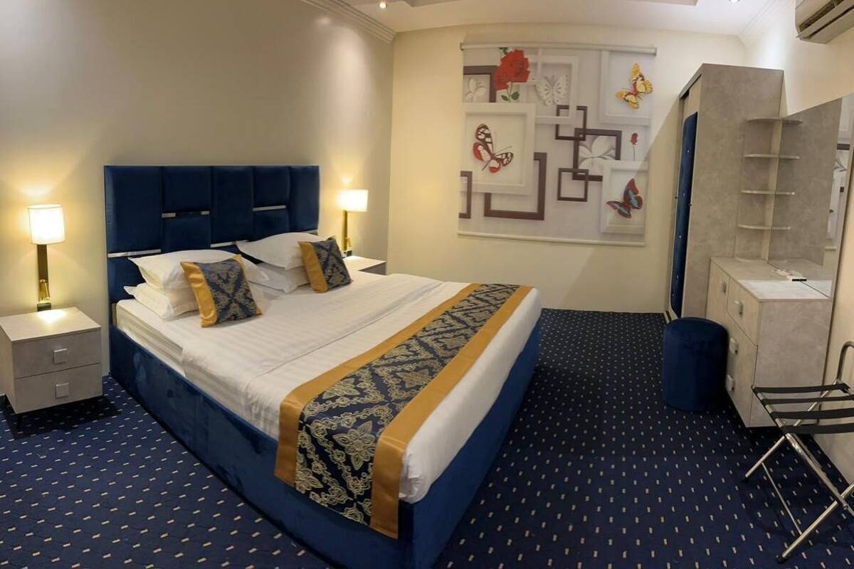 A neatly arranged hotel room with a large bed, bedside lamps, a wall-mounted shelf, and a compact seating area.
