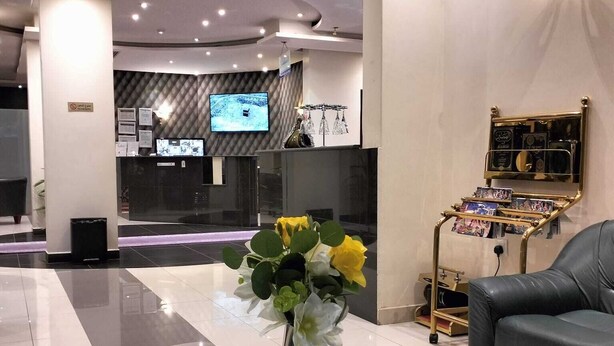 Eine moderne Lobby mit einer Rezeption, einem Fernsehbildschirm, einer Blumenkomposition, einer Papiertauschbox und einem Ledersofa.