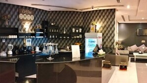 Ein modernes Café mit einer schwarzen Theke, Regalen mit Kaffeetassen, einem Automaten für Kinder Schokolade und einer Sitzecke mit einer Couch und Couchtisch.