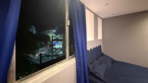 Een slaapkamer met een bed, een raam met gordijnen en uitzicht op een stadsbeeld 's nachts.