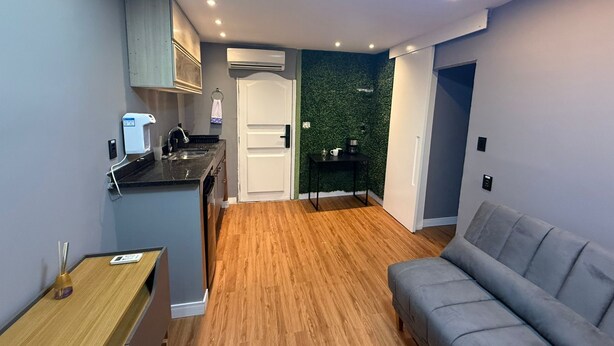 Een compacte leefruimte met een kitchenette, een grijze bank en een groene wand.