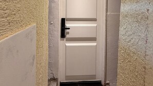 Een smalle gang met een witte deur, gestructureerde wanden en een plafondlamp.