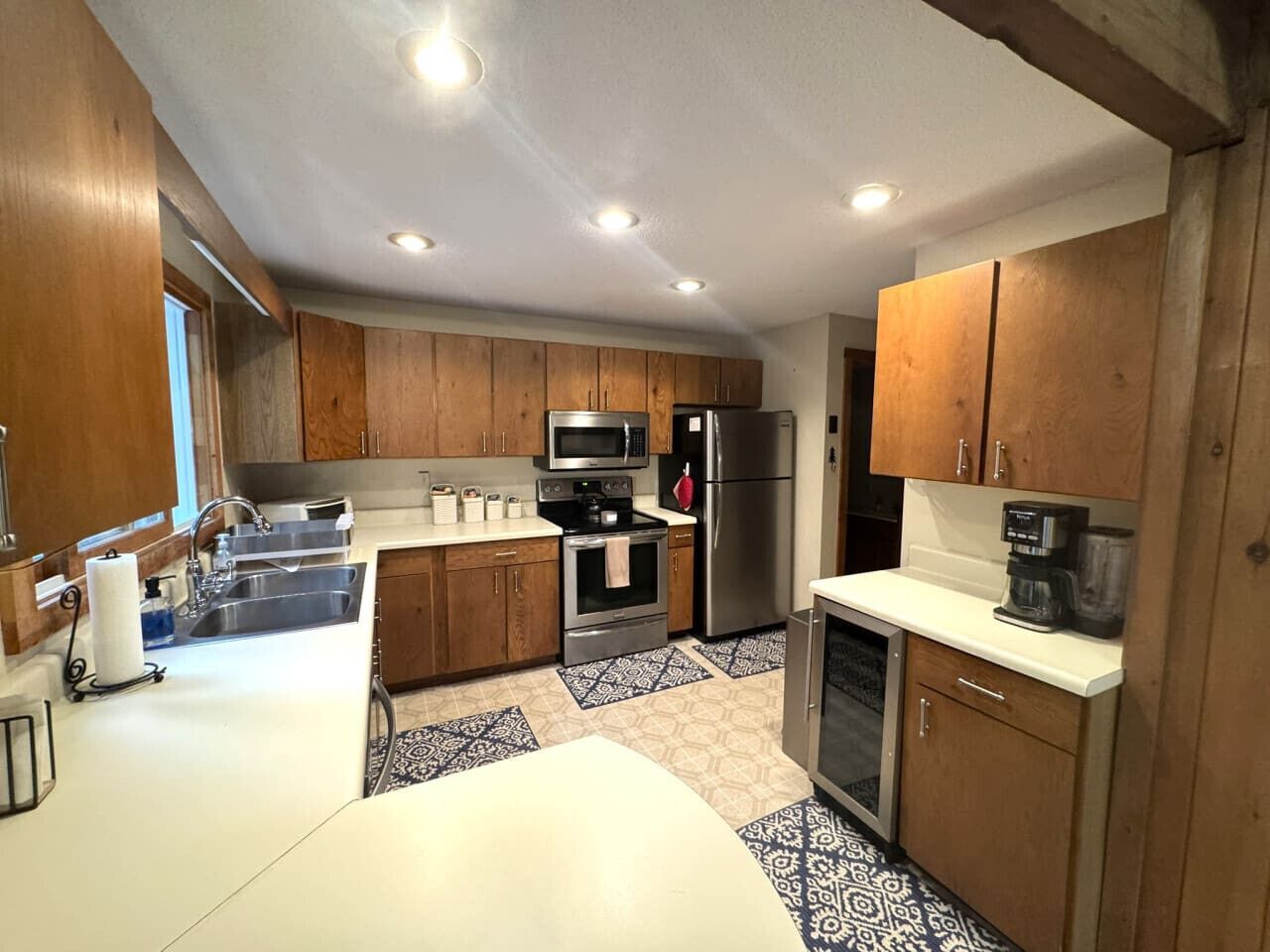 A modern kitchen with wooden cabinets, stainless steel appliances, a white countertop, and patterned floor tiles.