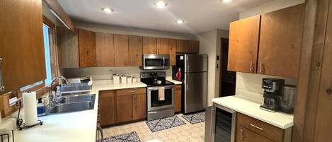 A modern kitchen with wooden cabinets, stainless steel appliances, a white countertop, and patterned floor tiles.