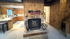 Una sala de estar acogedora con chimenea, paredes de madera y una zona de cocina al fondo.