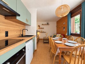 Een moderne keuken met houten keukenkastjes, een inbouwvaatwasser en een eethoek met een houten tafel en stoelen.