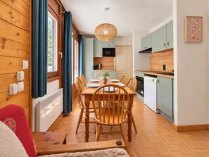 A modern kitchen with wooden cabinets, a dining table with chairs, and a hanging light fixture. - Cozy apartment with large terrace at the foot of the slopes (Flumet)
