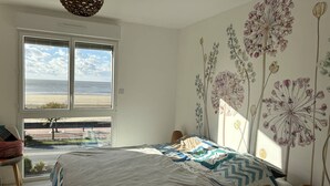 A bedroom with a large bed, a view of the beach, and a wall with floral wallpaper. - Apartment T4 - 6 ppl - Parking - Sea View in St Georges de Didonne (ST GEORGES DE DIDONNE)