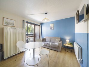 Une pièce comprenant une table ronde, deux chaises, un canapé, un ventilateur de plafond, un radiateur et une fenêtre avec des rideaux.