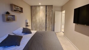 Un dormitorio moderno con cama, mesita de noche, lámpara, televisor y armario.