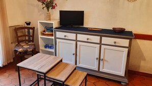 Ein Zimmer mit Holztisch, einem Stuhl, einem Fernseher auf einer Kommode und Dekoration an der Wand.