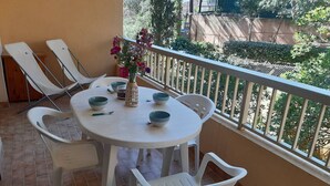 Ein Balkon mit einem runden Tisch, weißen Plastikstühlen und einer Vase mit Blumen.
