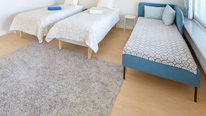 Ein modernes Schlafzimmer mit zwei Einzelbetten, einem Schlafsofa, einem kleinen runden Tisch und einem großen Fenster mit Vorhängen.