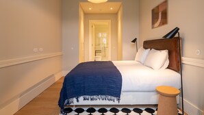 Un dormitorio con cama, mesita de noche, lámpara y vista al pasillo.