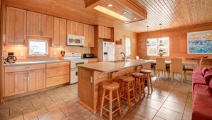 Een moderne keuken met houten kasten, een centraal eiland met krukken, en een eethoek met een rode bank.