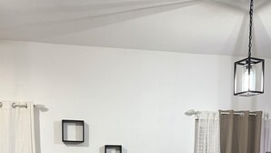 Ein modernes Wohnzimmer mit einem grauen Sofa, einem Esstisch mit Stühlen und einer Vase mit weißen Blumen. An der Wand hängen gerahmte Bilder und eine Pendelleuchte.