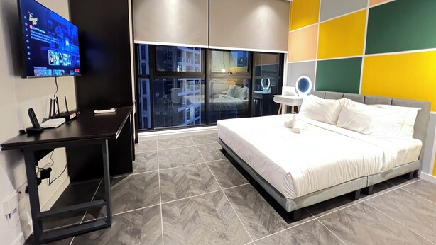 A modern hotel room with a large bed, a desk with a flat-screen TV, and a view of the city through large windows. - SCARLETZ SUITES KLCC BY LLP (Kuala Lumpur)