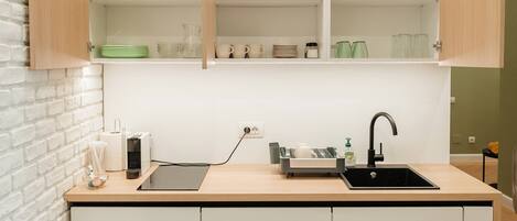 Una cocina compacta con armarios blancos, un lavamanos negro y una encimera de madera.