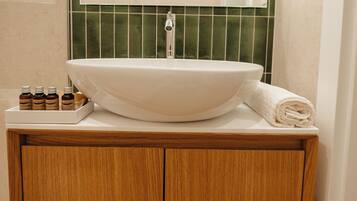 Bagno con lavabo bianco, mobile contenitore in legno, schienale rivestito in piastrelle verdi e uno specchio sopra il lavabo.