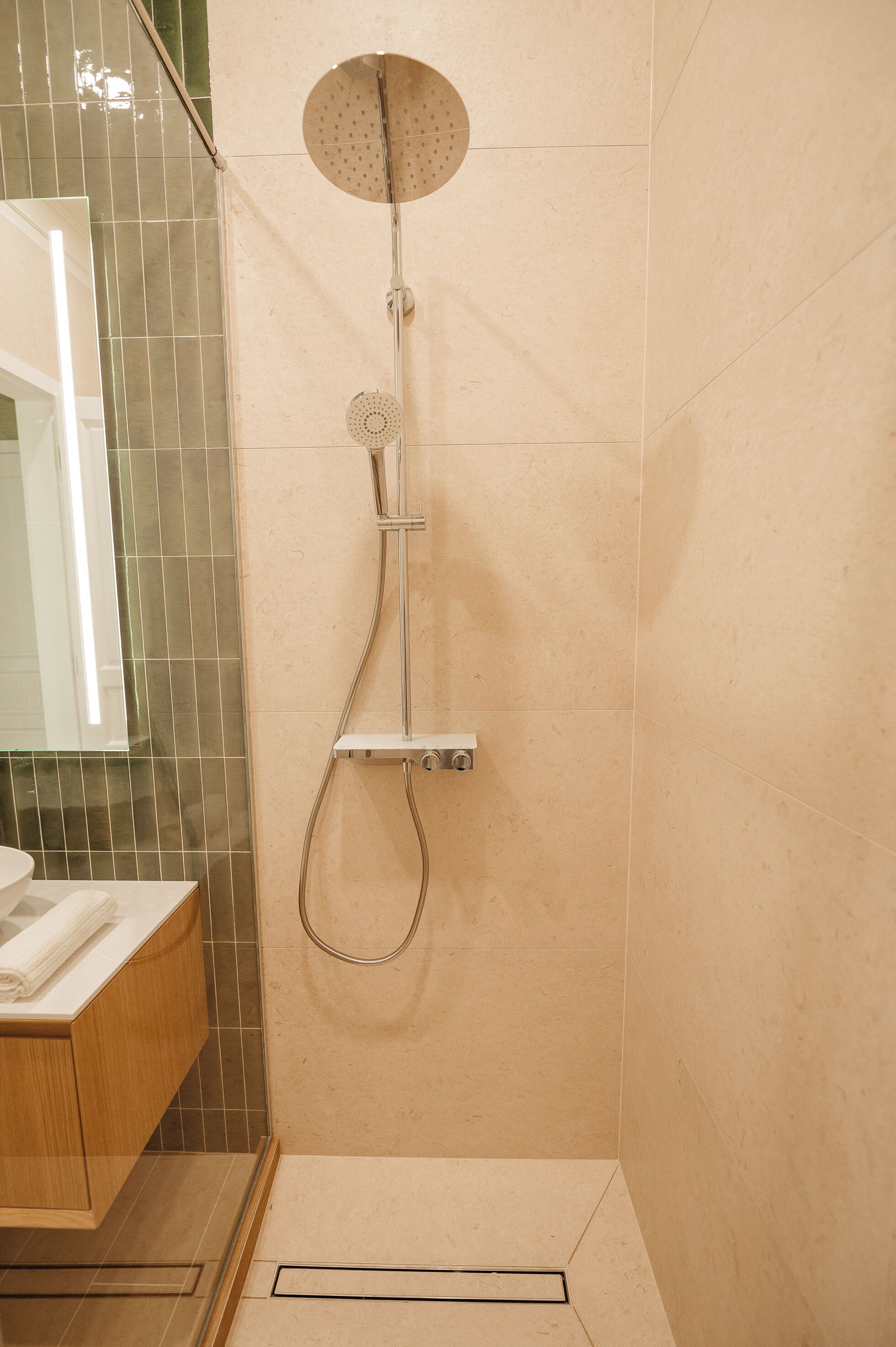 A shower with a handheld showerhead and a wall-mounted faucet, a wooden vanity with a towel, and a mirror.