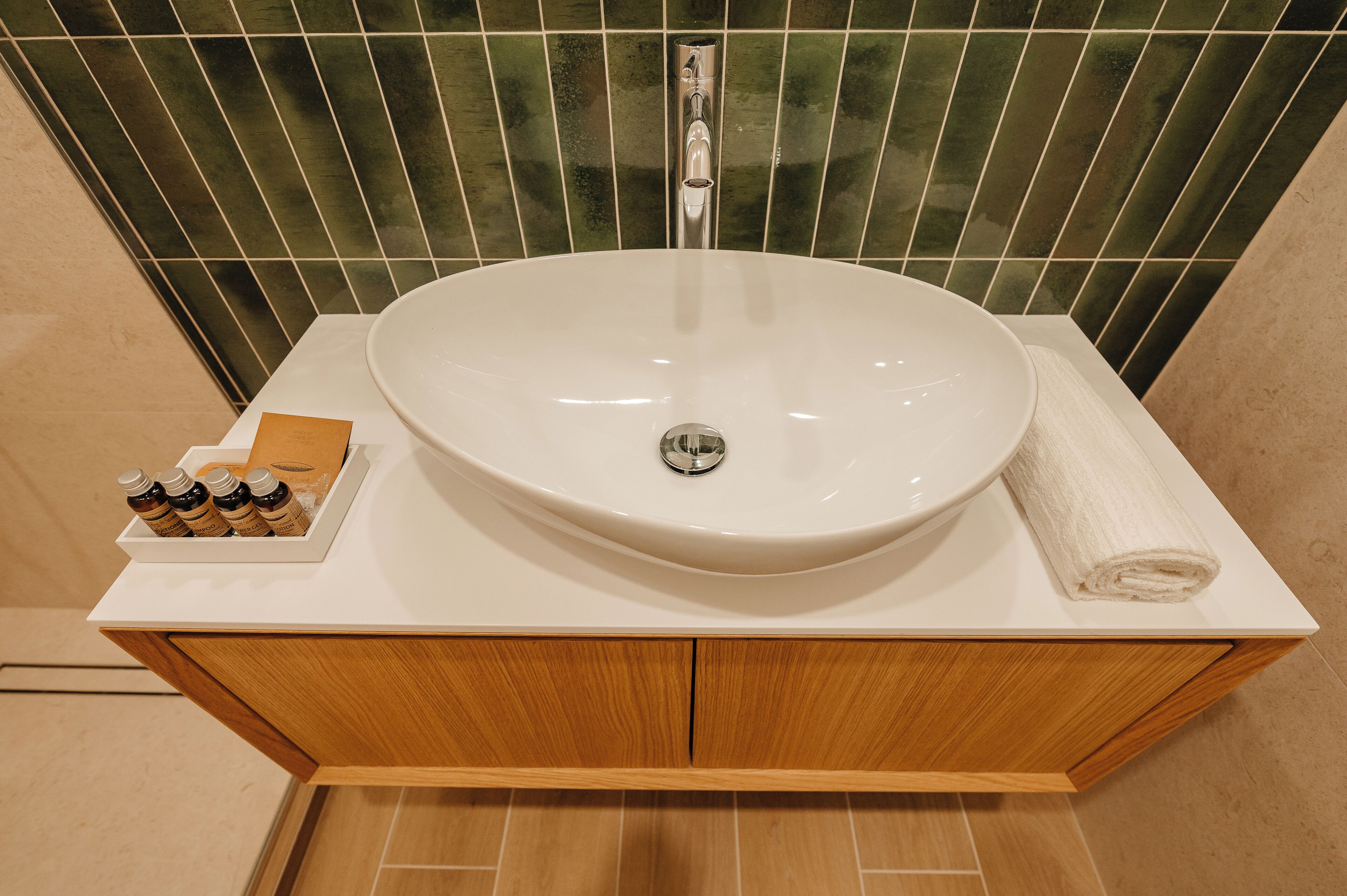 A bathroom with a white sink, wooden cabinet, and green-tiled wall.