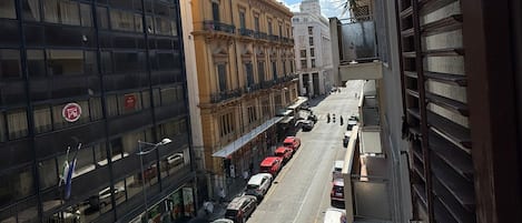 Vista de una calle con una mezcla de edificios modernos e históricos, incluyendo un edificio con grandes ventanales y una fachada clásica con balcones.