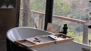 Ein Badezimmer mit einer Badewanne, einer Holzbank und Blick auf eine gebirgige Landschaft durch ein großes Fenster.