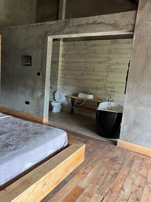 A room with a bed, wooden flooring, a bathroom with a toilet, sink, and bathtub.