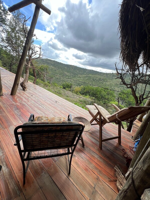 A wooden deck with a bench and two lounge chairs overlooking a hilly landscape.