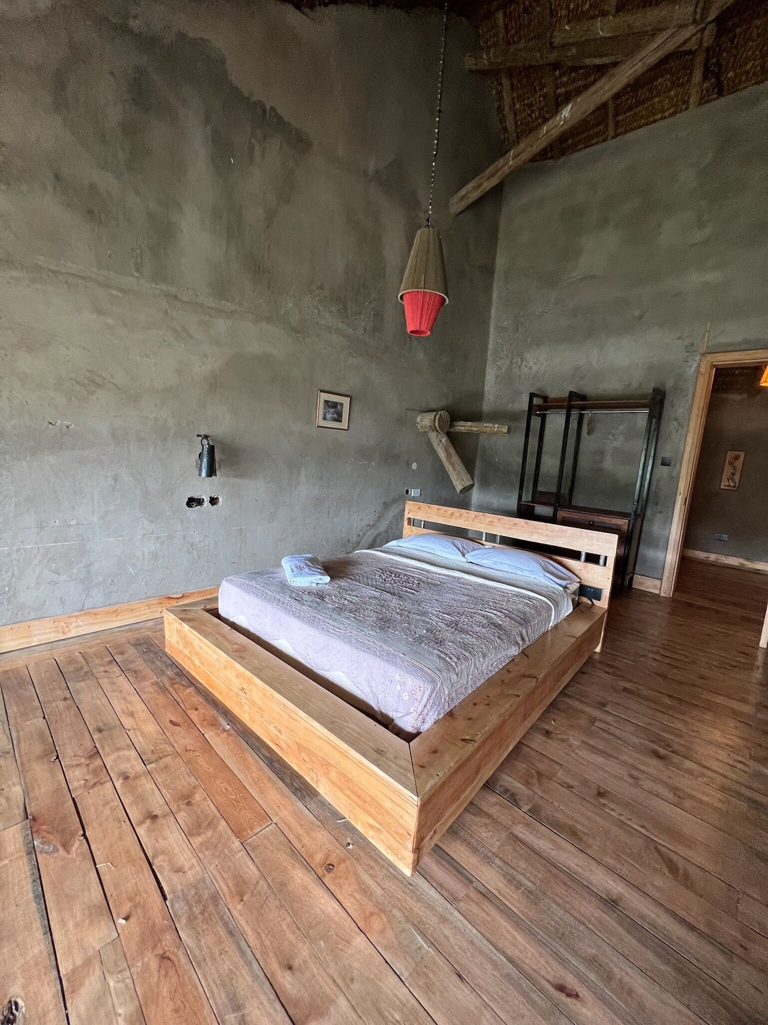 A wooden bed in a room with a concrete wall and a hanging red object.