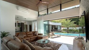 Un salon moderne avec un canapé en cuir, une table basse en verre et une vue sur une piscine et un espace de détente extérieur.